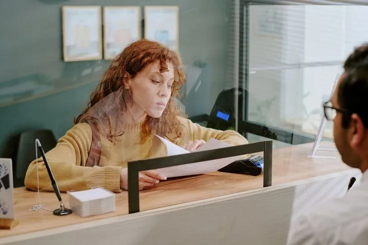 Atendente conferindo documento no balcão com cliente esperando do outro lado